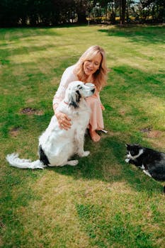 A woman smiling while sitting with her dog and cat on a sunny day in the garden.